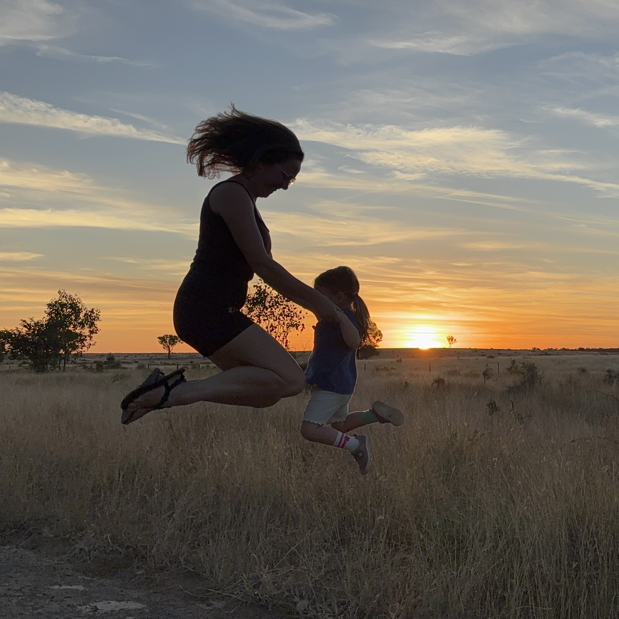 Mother lifting her child into the air at sunset